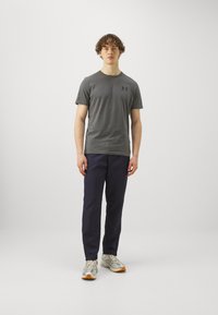T-shirt gris à manches courtes avec un logo subtil, associé à un pantalon bleu marine et des baskets gris clair avec des accents orange.