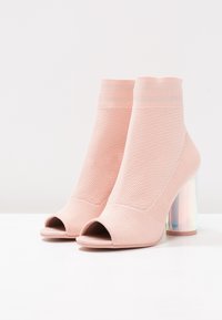 Botines rosas con punta abierta, parte superior de punto texturizado y un tacón grueso, claro e iridiscente. Suela lisa y parte superior elástica para un mejor ajuste.