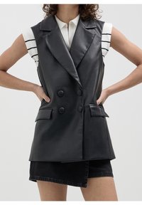 Svart läder dubbelt knäppt väst med notch-laplar, framfickor och en elegant design, bärs över en randig vit skjorta.