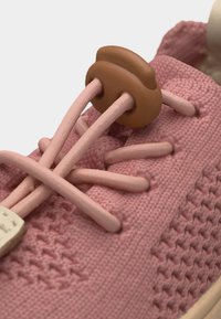 Gros plan sur une basket tricotée rose avec un verrou de lacet rond et doux marron assurant les lacets rose clair passés à travers des œillets en tissu.