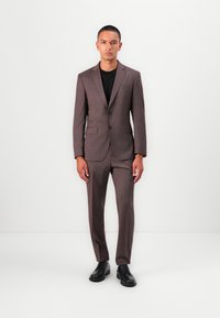 Completo a quadri marrone con vestibilità su misura, giacca monopetto, colletto a scollatura a V e pantaloni dritti abbinati a scarpe nere.