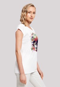 White t-shirt featuring a central skull graphic surrounded by colorful flowers. Short sleeves and a relaxed fit design. Soft cotton material.