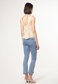 Top in lino beige con un corpetto aderente e orlo svasato, abbinato a jeans azzurri chiari e sandali bianchi con cinturini. Design minimalista, senza motivi.