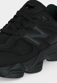 Baskets de sport noires avec mesh texturé, col rembourré, semelle épaisse, lacets noirs et grand logo réfléchissant de la marque sur le côté.