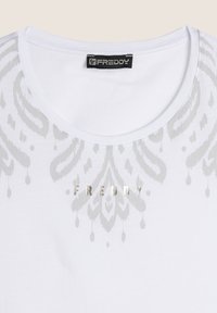 T-shirt bianca con scollatura rotonda, caratterizzata da un motivo damascato argento e il nome del marchio "FREDDY" in lettere metalliche al centro.