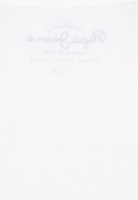 Bílá bavlněná tkanina s hladkou texturou, na které je v horní centrální části jemný šedý potisk značky a pokynů k údržbě.