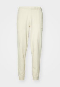 Cream-colored sweatpants made of soft fabric with an elastic waistband and cuffs. Features a small logo patch on the left hip.