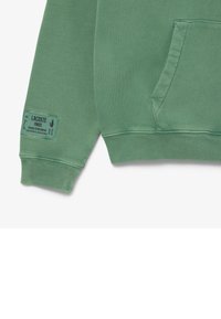 Grüner Baumwollpullover mit einer Vorderseite-Tasche, gerippten Bündchen und einem gewebten Etikett mit Markeninformationen. Glatte Textur, lässiges Design.