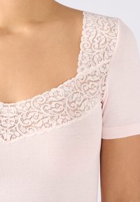 Top de manga corta rosa claro con un borde de encaje alrededor del escote cuadrado, con una textura suave y acanalada y un diseño ajustado.