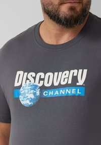 Graues T-Shirt mit dem Text "Discovery Channel" in Weiß und Blau, in der Mitte mit einer Grafik der Erde. Standard Rundhalsausschnitt-Design.