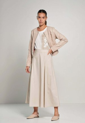 Giacca di pelle beige, camicia bianca con motivo floreale e lunga gonna beige. Tessuto liscio e design minimalista, completato da scarpe flat.