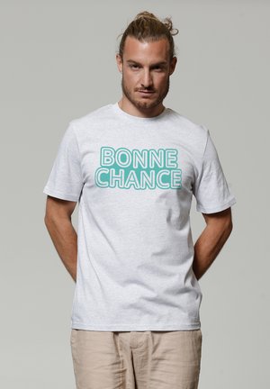 Hellgraues Baumwoll-T-Shirt mit kurzen Ärmeln, das den Text "BONNE CHANCE" in fettem Türkis aufweist. Glatte Textur mit Rundhalsausschnitt.