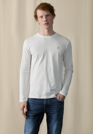 Witte langemouw t-shirt van katoen, met een ronde hals en een klein geborduurd logo op de linkerborst, gedragen met blauwe jeans.