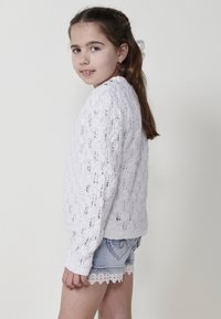 Un pull en tricot blanc avec un motif en dentelle texturé, associé à un short en denim bleu avec une bordure en dentelle festonnée au bas.