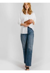 Vit skjorta med knappar, lös passform; blåa högmidjade jeans; håller en brun läderclutch; minimalistisk design; svarta platta sandaler.