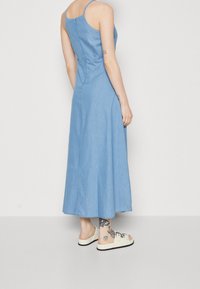 Vaaleansininen farkkumaksimekko ohuilla olkaimilla, kiristetty vyötärö, sivurei'ät ja sileä pinta. Yhdistetty pukeutumiskenkien kanssa.