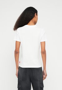 Λευκό βαμβακερό t-shirt με στρογγυλή λαιμόκοψη και κοντά μανίκια. Στο πίσω μέρος διαθέτει μια μικρή κόκκινη ετικέτα λογότυπου στο τελείωμα. Ομαλή υφή, κανονική εφαρμογή.