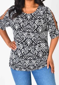 Černobílý vzorovaný top s výřezovými rukávy, kulatým výstřihem a krátkými rukávy. V kombinaci s modrými džíny, které mají uvolněný střih.