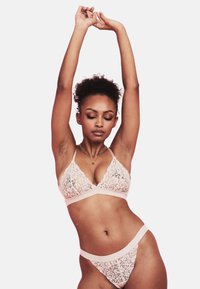 Set di bralette in pizzo e perizoma di un delicato rosa pallido, caratterizzato da intricati motivi floreali e bande elastiche morbide per il massimo comfort. Il reggiseno ha spalline regolabili.