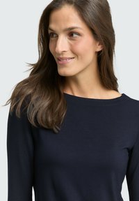 Langsleeve marineblauwe top van zacht materiaal met een ronde halslijn en een gladde textuur. Kenmerkt zich door gestikte details langs de halslijn.