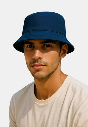 Chapeau seau bleu marine en tissu texturé avec un large bord incliné vers le bas, porté par une personne vêtue d'une chemise de couleur claire.