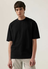 Tricou negru din bumbac supradimensionat, cu guler rotund și mâneci scurte. Materialul pare neted, fără modele sau embellishments vizibile.