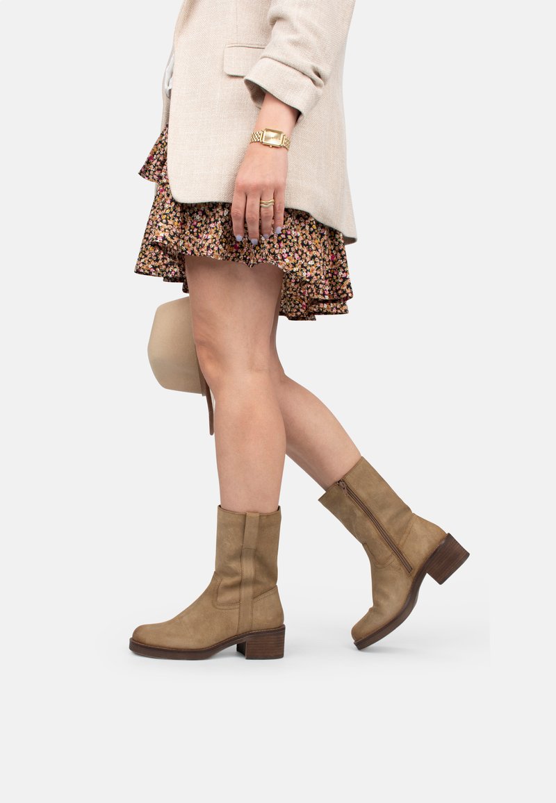 Botas de tobillo de cuero marrón claro con punta redondeada, un tacón cuadrado de 5 cm y cremallera lateral. El diseño presenta detalles cosidos y una textura suave.