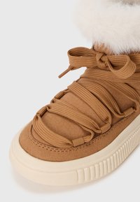Baskets montantes en suede marron avec semelle épaisse crème, lacets détaillés et col en fourrure blanche. Surface texturée avec des détails de couture.
