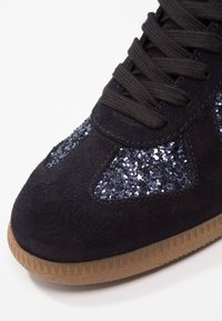 Baskets en daim noir avec accents en sequins, semelle en caoutchouc texturée et lacets plats noirs. Dotées d'un col rembourré et d'un motif de bande de roulement triangulaire.