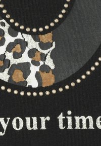 Schwarzer Stoff mit einem Leopardenmuster in Weiß- und Brauntönen, akzentuiert mit metallischen Nieten und silbernem Text "deine Zeit."