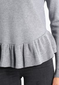 Maglione grigio con dettaglio a peplo a coste e maniche lunghe, realizzato in un morbido materiale a maglia. Abbinato a jeans scuri.