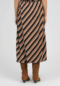 Jupe maxi avec un motif de rayures diagonales noires, brunes et blanches ; tissu léger avec une taille froncée ; associée à des bottes de cowboy brunes.
