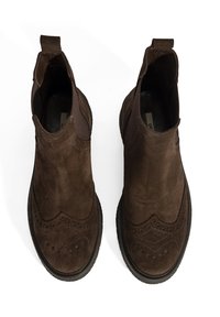 Bottines en suede brun avec des détails de brogue, des panneaux latéraux élastiques et des languettes de tirage. Semelles en caoutchouc plates et une forme de bout légèrement arrondie.