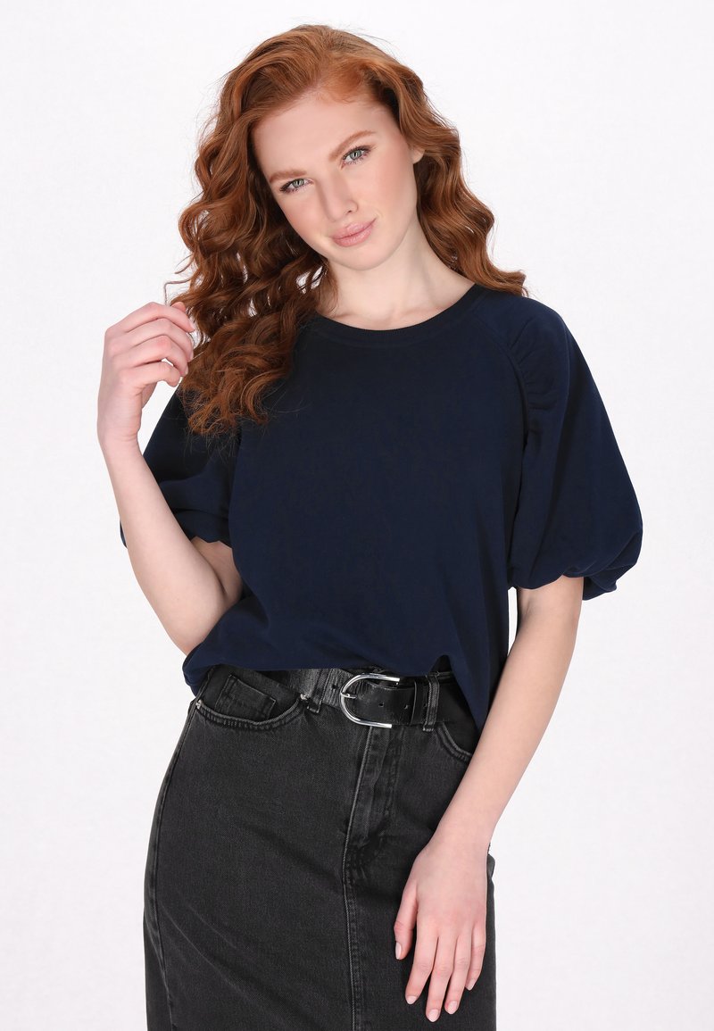 Top blu navy a maniche corte con spalle a palloncino, indossato con una gonna in denim nera a vita alta con cintura. Tessuto morbido e vestibilità rilassata.
