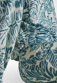 Bedrucktes Stoffoberteil mit grünen und blauen botanischen Mustern, weicher Textur und gestaffeltem Volantsaum. Mischung aus hellen und dunklen Farben.