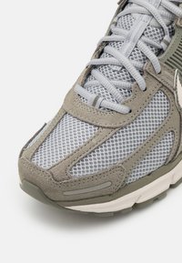 Baskets grises et vert olive avec tige en maille, accents en daim et semelle rembourrée. Détails réfléchissants sur les côtés.