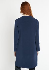 Robe longue bleu marine à manches longues avec un col rond simple et une coupe droite. Texture lisse, longueur genou, avec un motif légèrement chiné.