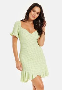 Green dress featuring a fitted design, short puff sleeves, V-neckline, and ruffled hem, adorned with a polka dot pattern.