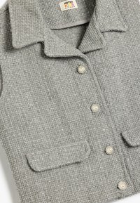Grå tweed vest med en tekstureret finish, der har perleknapper, en krave og to frontlommer. Materialet inkluderer metalliske tråd accenter.