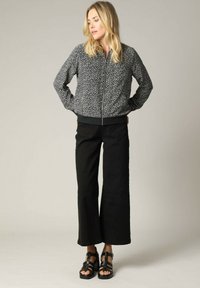 Zwart-witte gestructureerde bomberjack met een rits aan de voorkant, geribbelde manchetten en zoom, gecombineerd met wijde zwarte broeken en zwarte sandalen met bandjes.