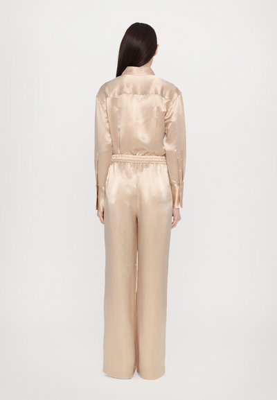 Satin pajama set in light beige, featuring a collared shirt and elastic waistband pants with a relaxed fit and smooth texture.