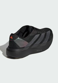 Zapatilla deportiva negra con parte superior de malla, tres rayas prominentes y un talón texturizado. Presenta una suela gruesa etiquetada como "LIGHTSTRIKE PRO".