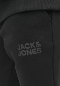 Melnas sporta bikses, kas izgatavotas no mīksta auduma, ar ribotu jostasvietu un diskretu pelēku logo "JACK&JONES" kreisajā augšstilbā.