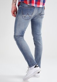 Persona que lleva unos vaqueros ajustados de color azul claro, una camisa a cuadros roja y azul, y zapatillas Nike blancas con detalles en negro.