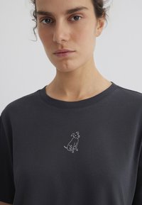 Dark gray cotton t-shirt featuring a white, simple line drawing of a sitting dog on the chest, with a round neckline and short sleeves.