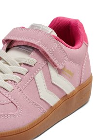 Roze suède sneaker met witte leren accenten, voorzien van een klittenbandsluiting, een getextureerde buitenzool en gestikte details. Zachte voering aan de binnenkant.