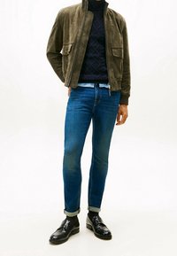 Vihreä mokkajakku vetoketjulla, laivastonsininen neulepusero, siniset slim fit -farkut ja mustat kiillotetut loafer-kengät. Farkuissa on käänteet.