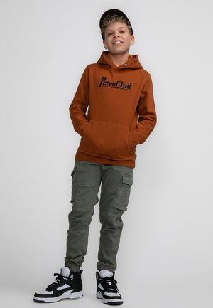 Felpa marrone con stampa "Petrol Ind", pantaloni cargo verdi e sneakers nere. La felpa ha una tasca frontale e un cappuccio regolabile con cordino.