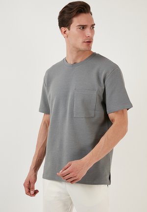 Grå kortærmet t-shirt med lomme; ribbet tekstur og rund hals; sideslidse detaljer; bæres med lyse bukser.