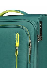 Valise turquoise avec un extérieur texturé, des accents de fermeture éclair jaunes, deux fermetures éclairs et une serrure à combinaison intégrée. Fini lisse, forme rectangulaire.